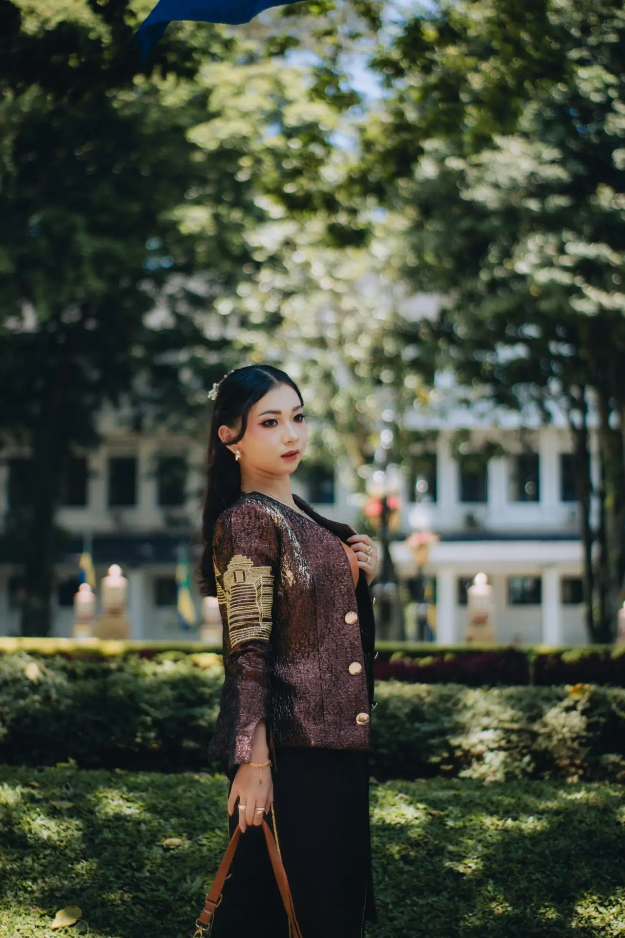 A woman in elegant traditional attire poses gracefully in a lush garden setting in Jawa Barat, Indonesia.
